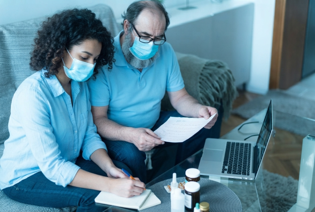A diverse team wearing blue masks and light blue attire collaborating on medical documents with a laptop and pill bottles in a sky blue-themed room