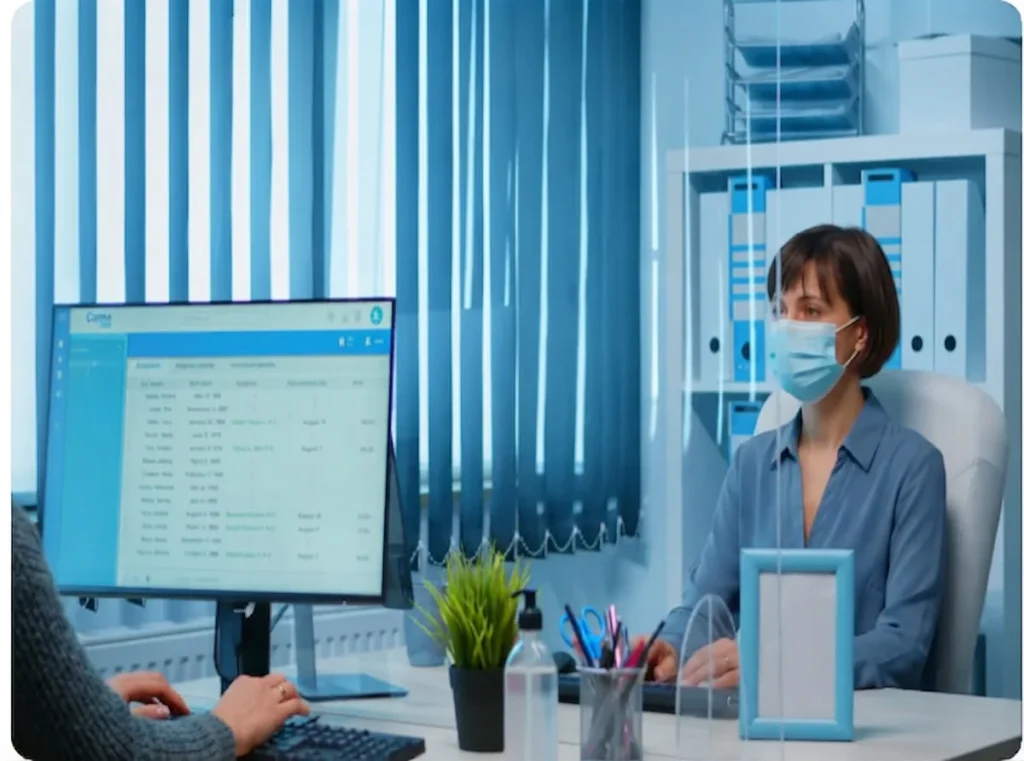 A woman with a long braid wearing a blue sweater sits at a desk with a laptop, checking a shipping invoice.