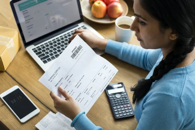 A black electronic calculator resting on a wooden desk next to financial papers.